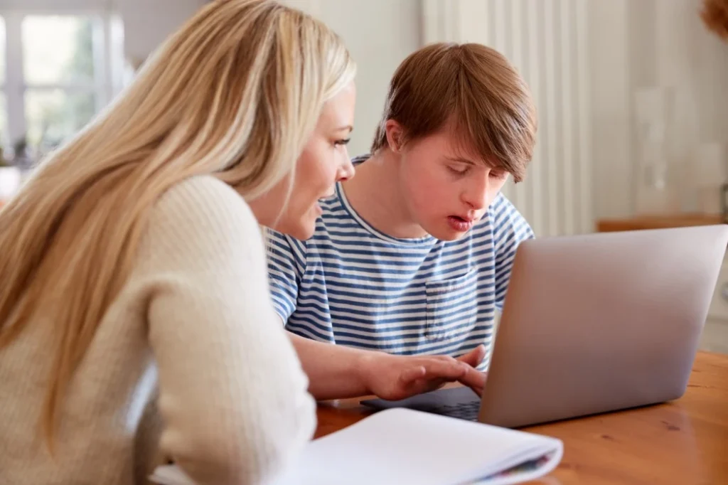 Disabled man with down syndrome using laptop with support coordinator