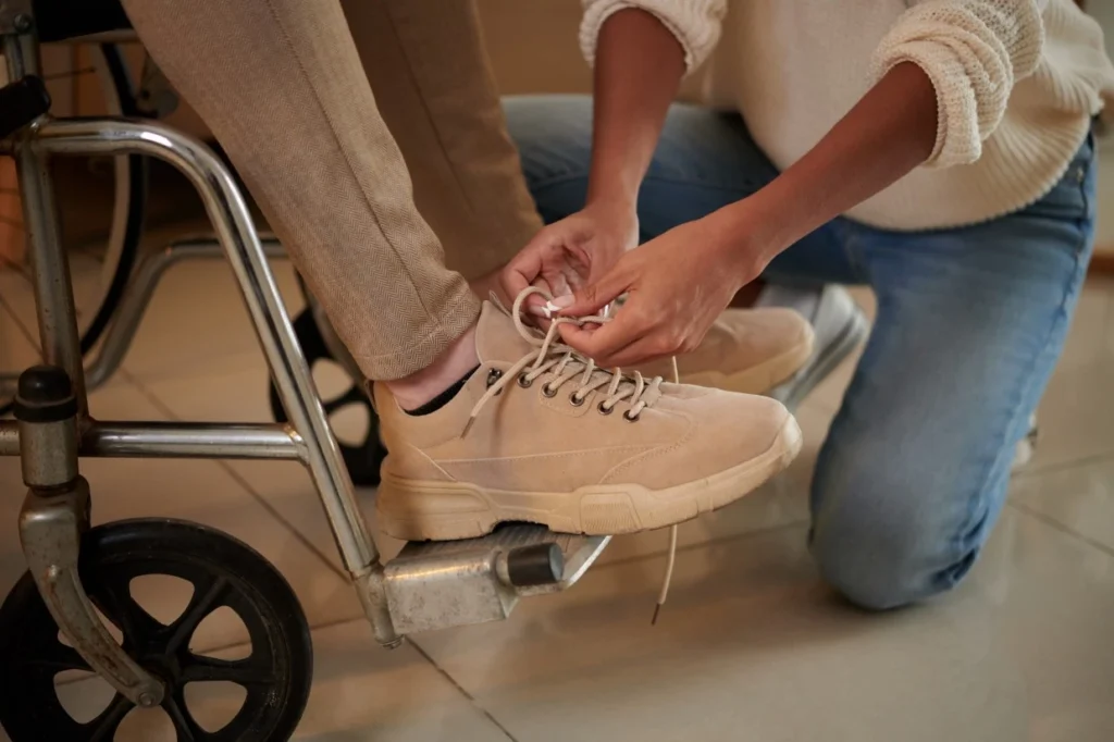 Support worker tying shoe laces for disabled man in wheelchair